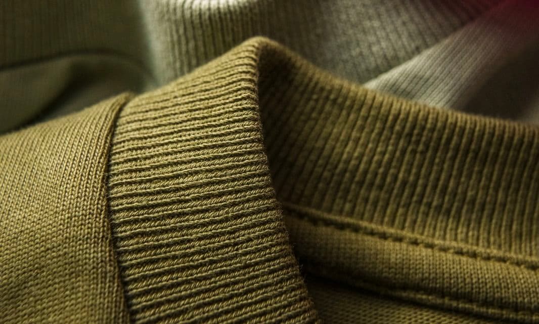 Close-up of a folded olive-green knit fabric with ribbed texture, showing detailed stitching, fabric quality, and soft material.