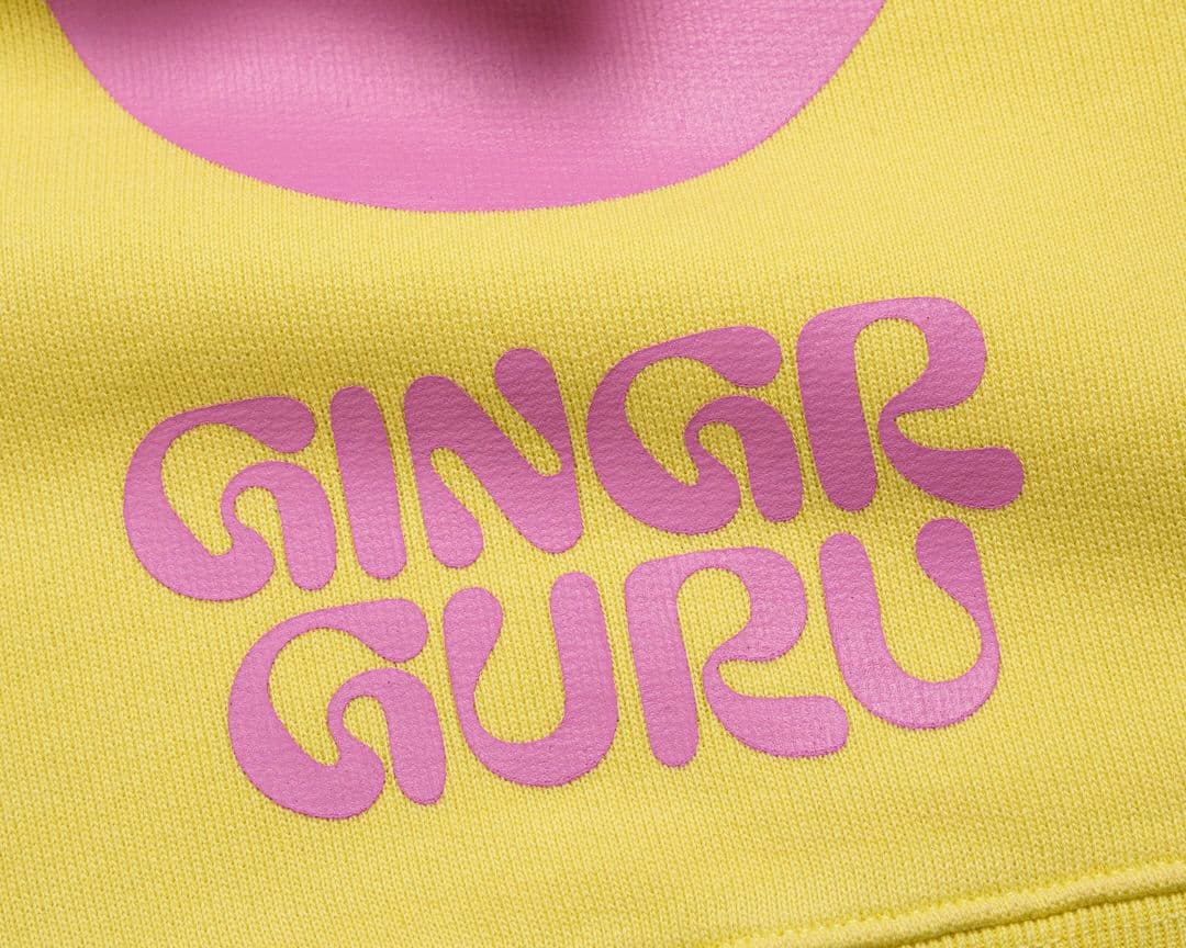 Close-up of yellow fabric with "GINGER GURU" in bold, pink, stylized text.