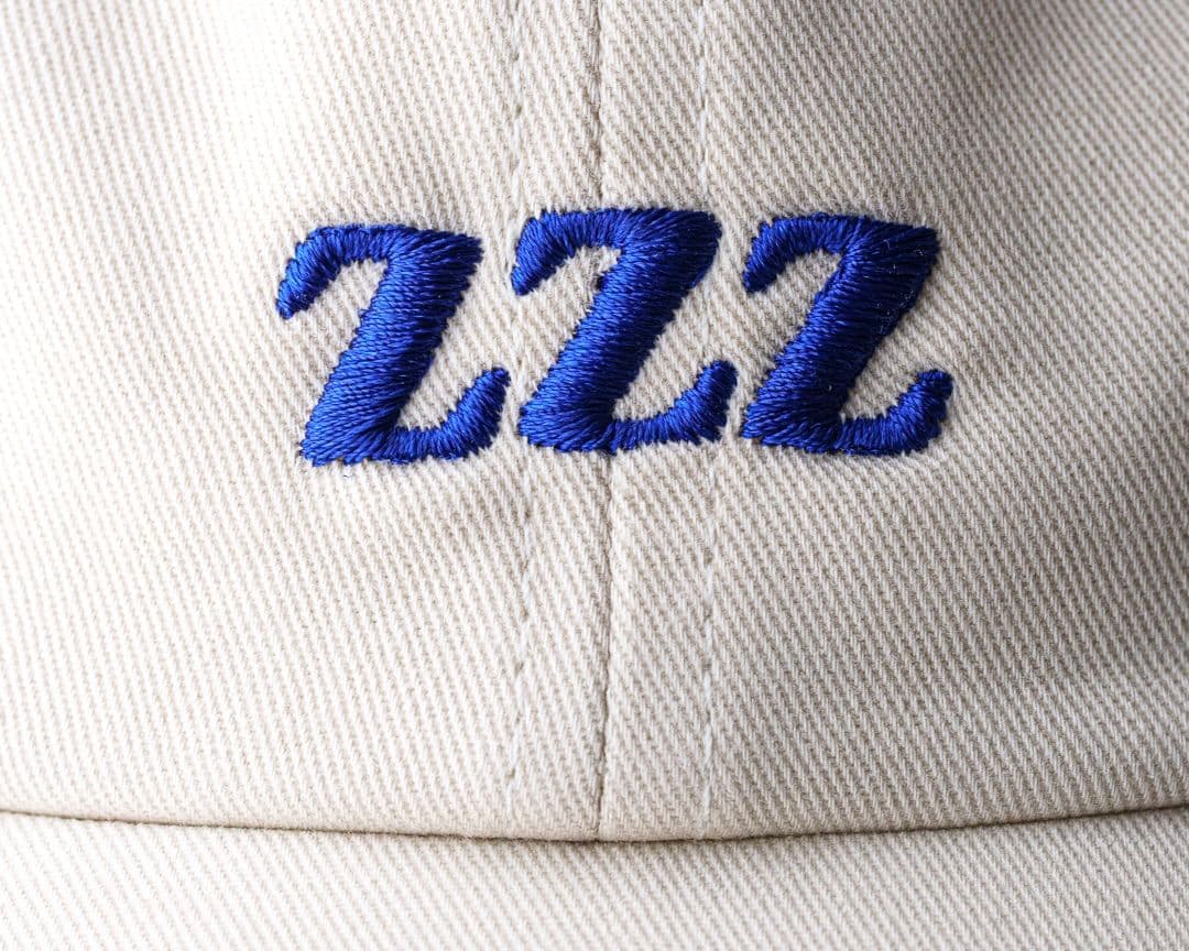 Close-up of a beige fabric cap with "ZZZ" embroidered in blue on the front.