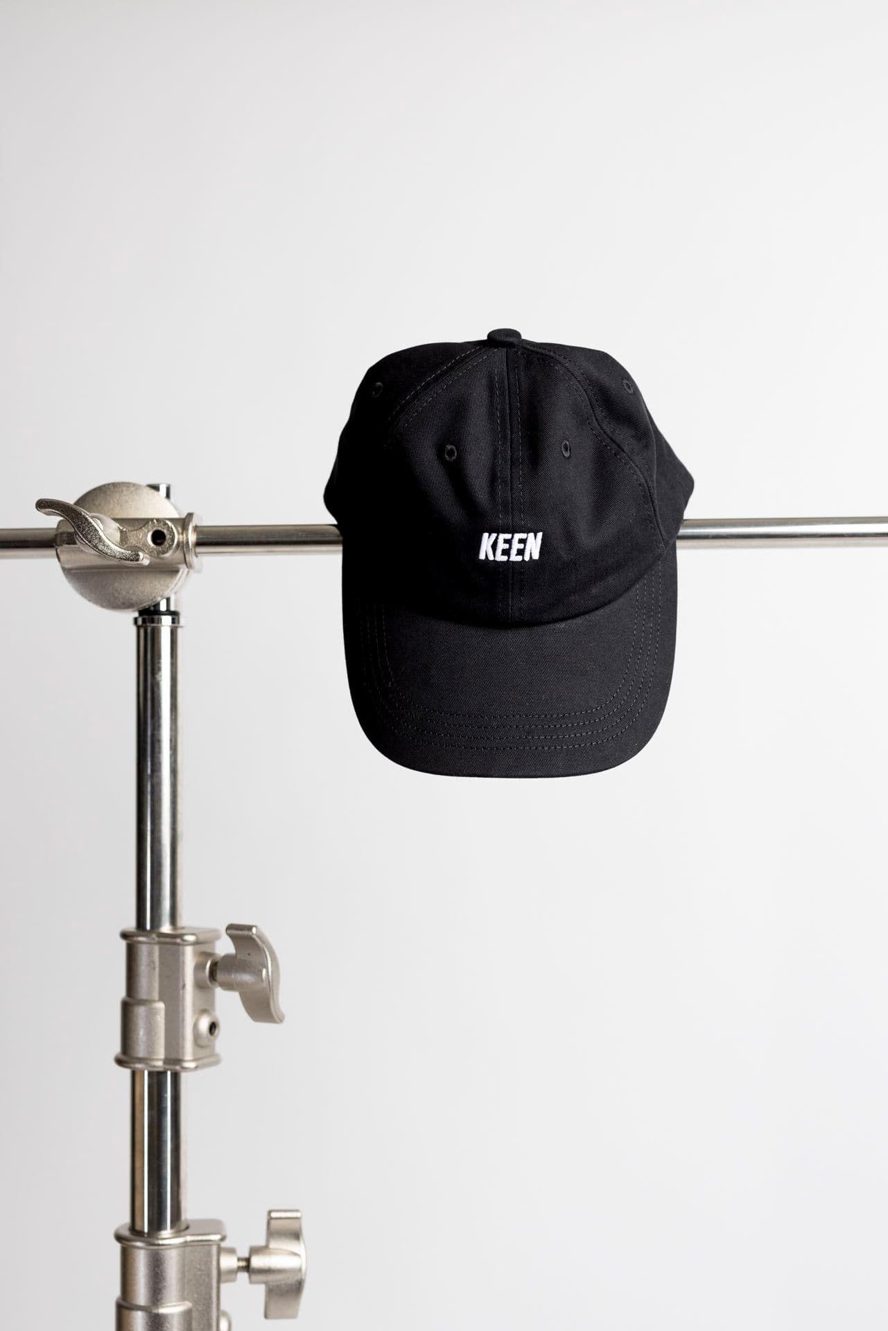 Black cap with "KEEN" logo, hanging on a metal stand against a plain white background.