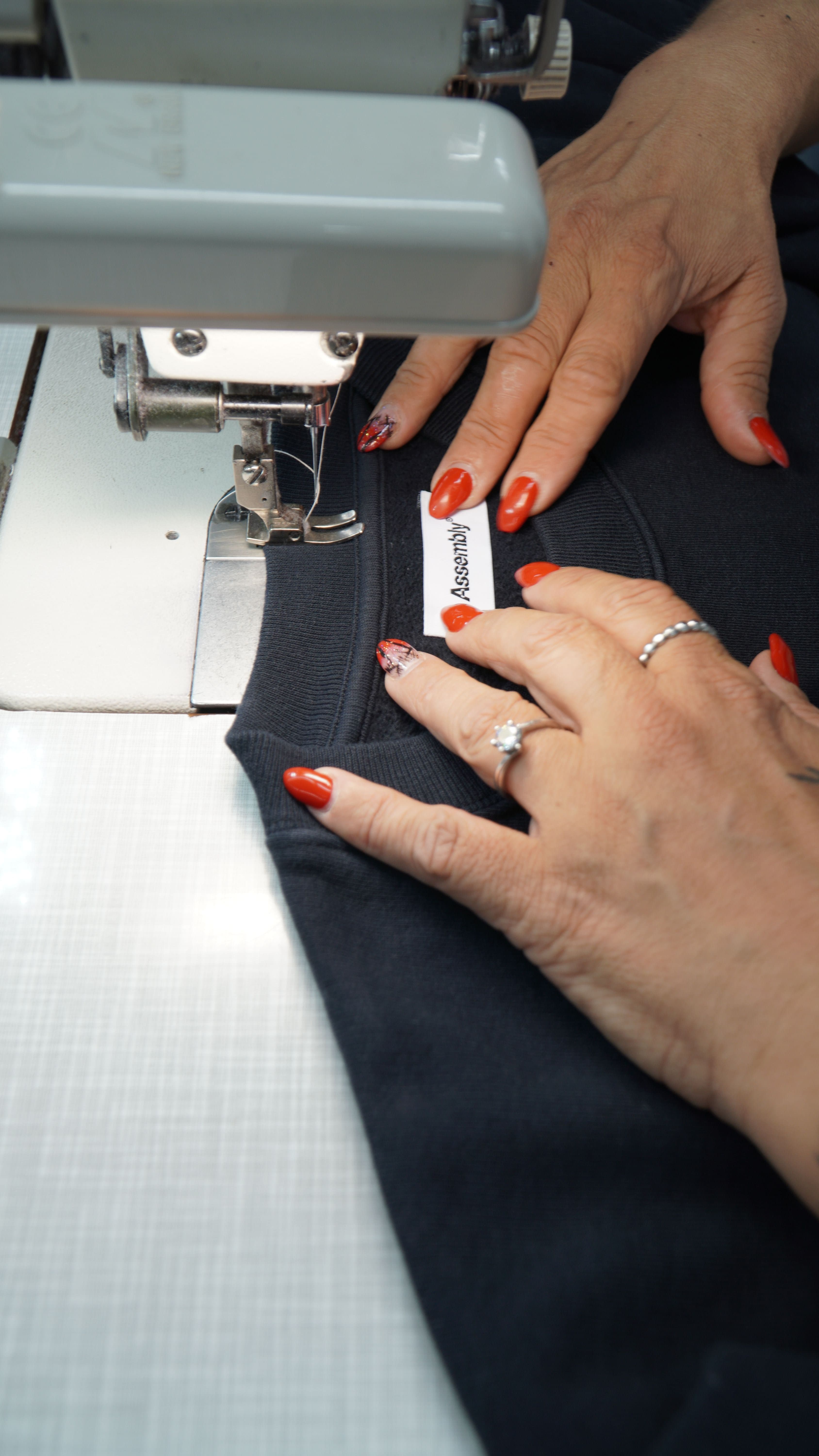 Hands sewing a woven neck label onto a black garment