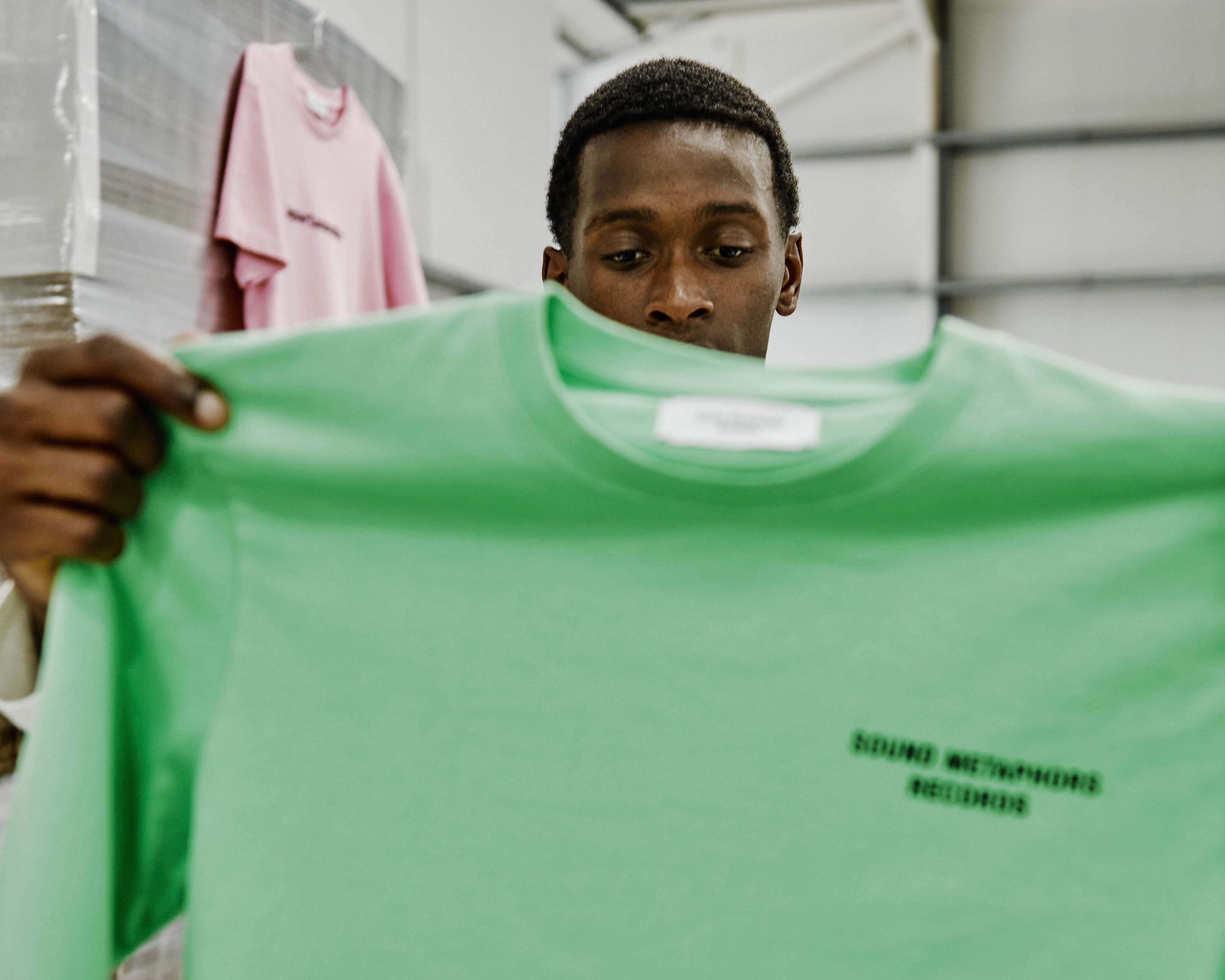 Person holding up a green sweatshirt inside a production facility