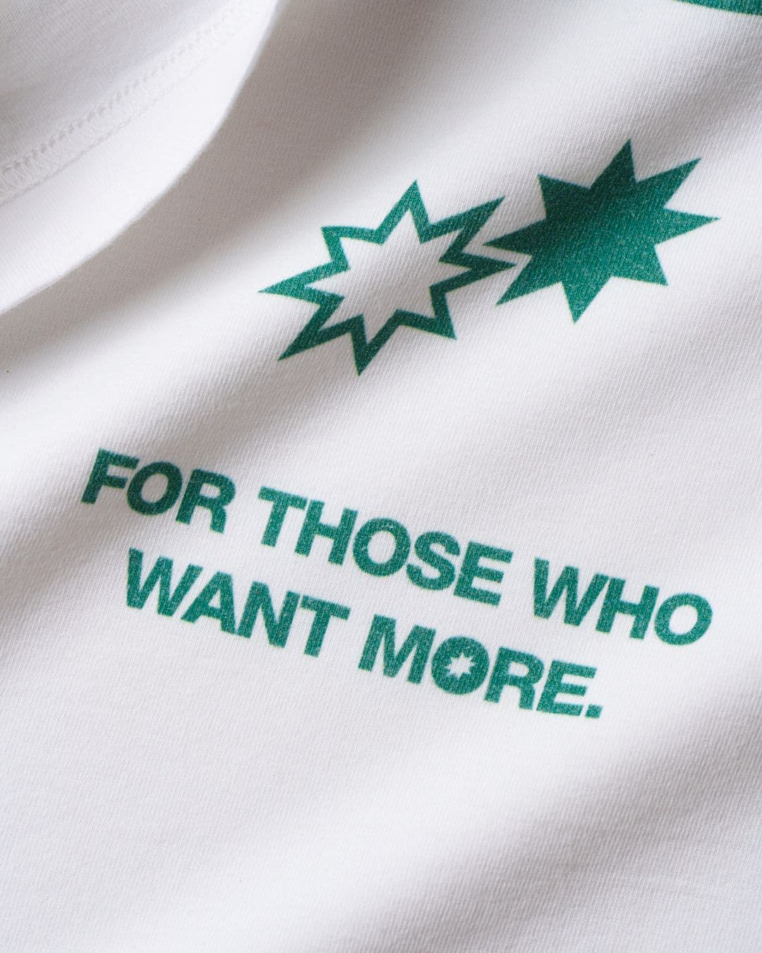 Close-up of DTG print on a white t-shirt with green stars and the text "For those who want more."
