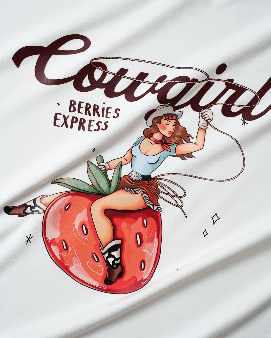 Close-up of DTF print on a white t-shirt featuring a colourful cowgirl illustration riding a strawberry with the text "Cowgirl Berries Express."