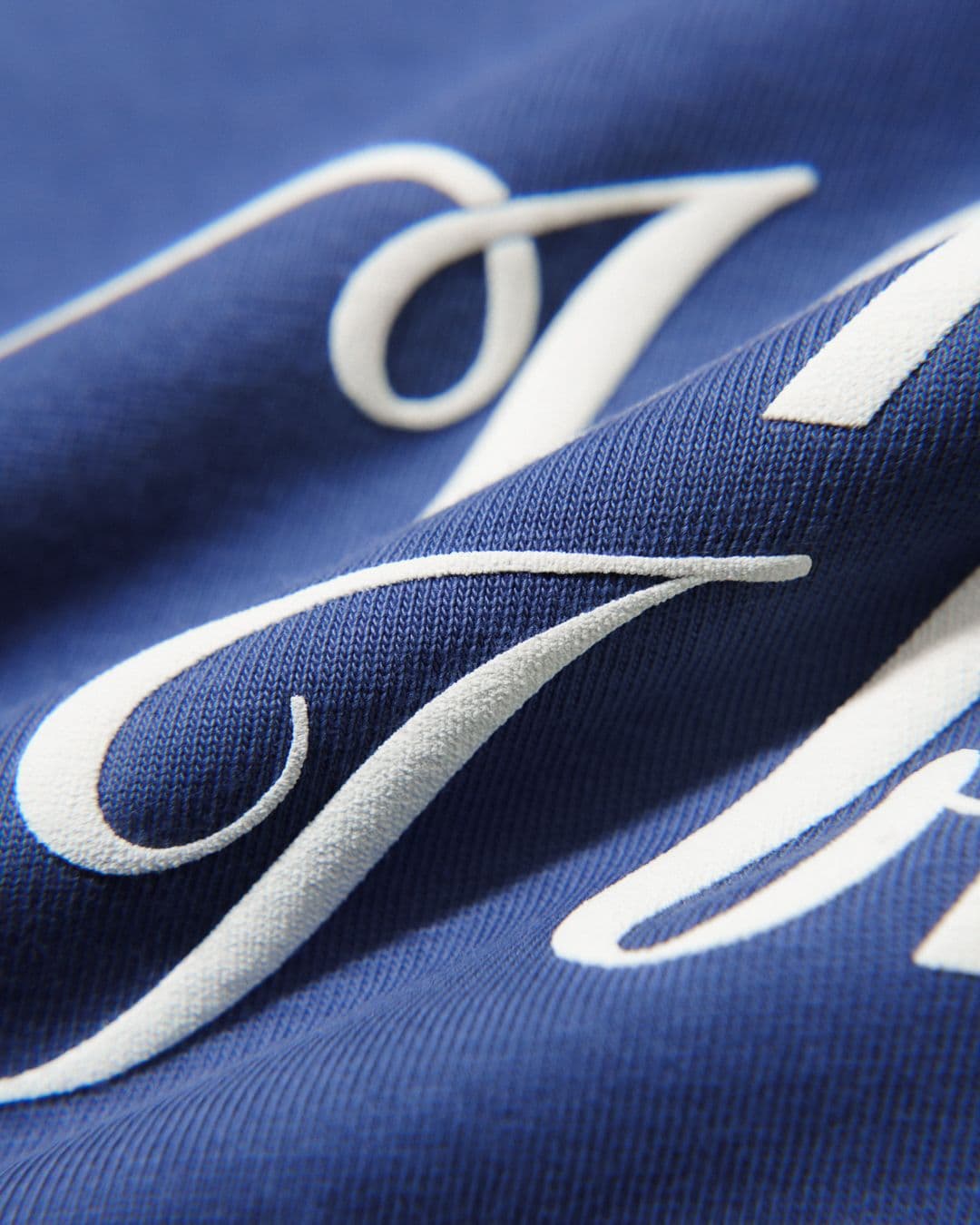 Close-up of white cursive text on a blue fabric, showing detailed texture and elegant curves of the lettering.