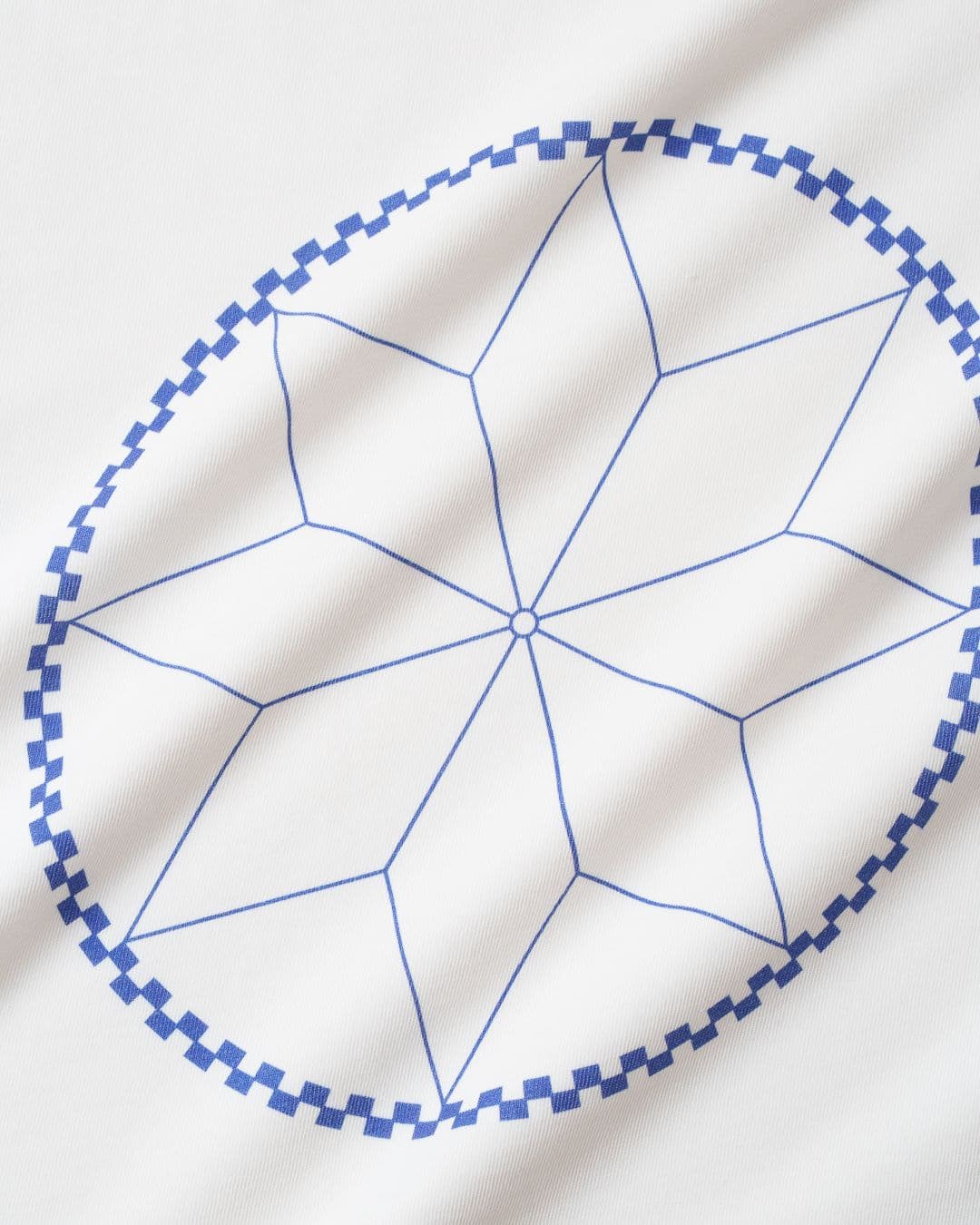 Blue geometric star pattern inside an oval with a checkered border on white fabric.