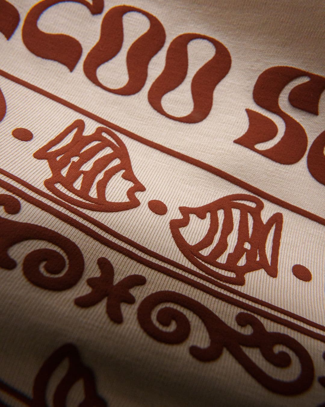 Close-up of puff print design with brown graphic shapes and fish motifs on cream fabric.