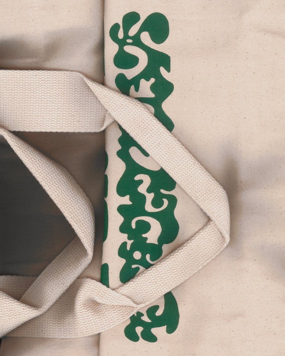 Close-up of cream tote bag with green printed design and woven handles.