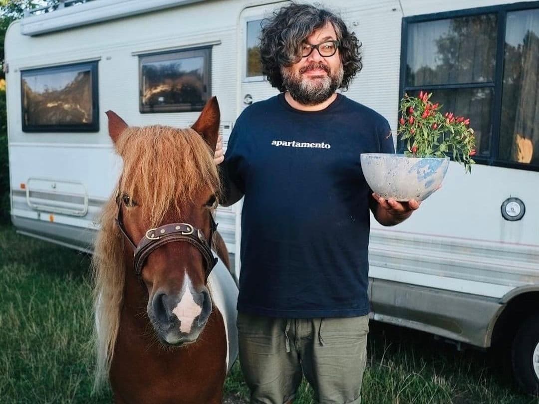 Man wearing an Apartamento custom t-shirt holding a plant next to a pony in front of a camper van
