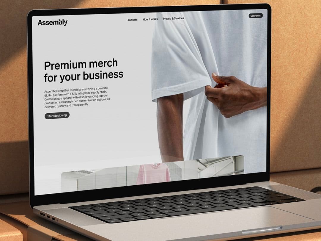 Laptop showing Assembly website with headline "Premium merch for your business" on screen