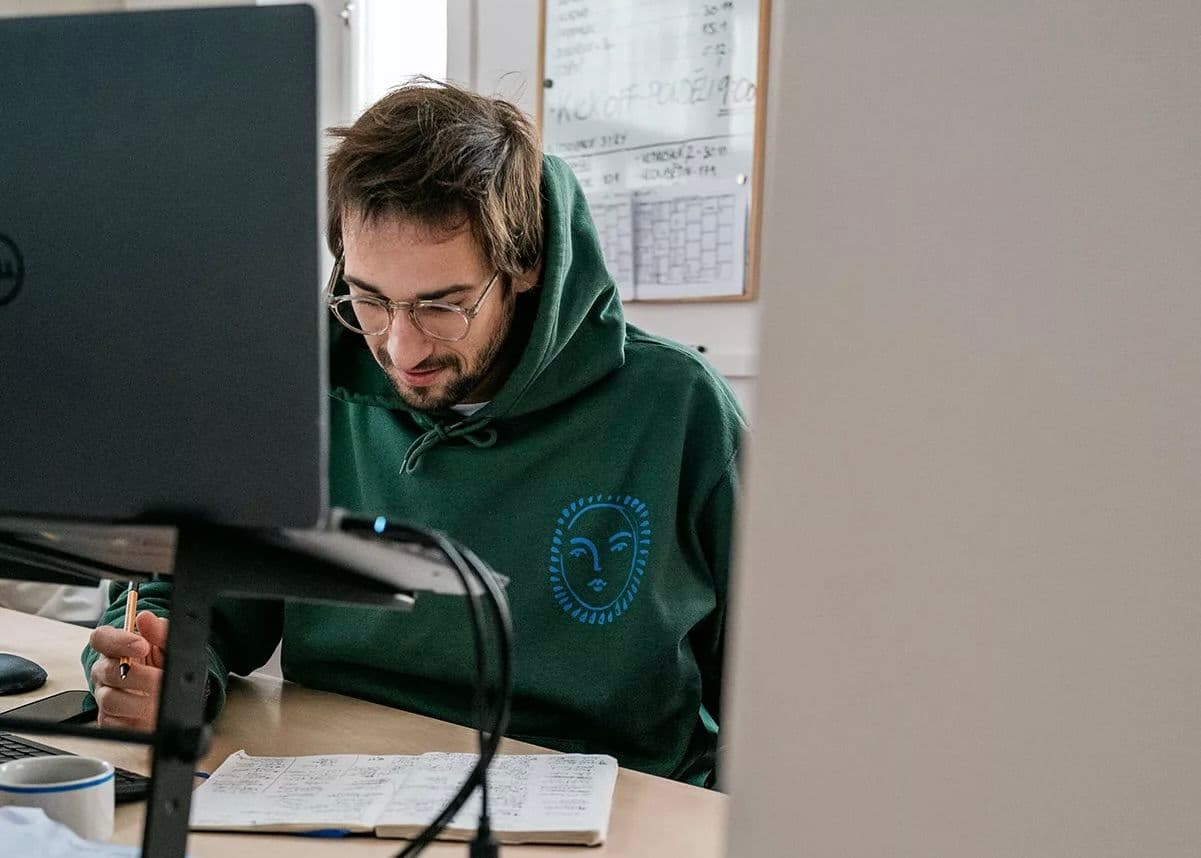 Team member at In August wearing a green garment dyed hoodie while working at a desk, showing the comfort and premium quality of office apparel.