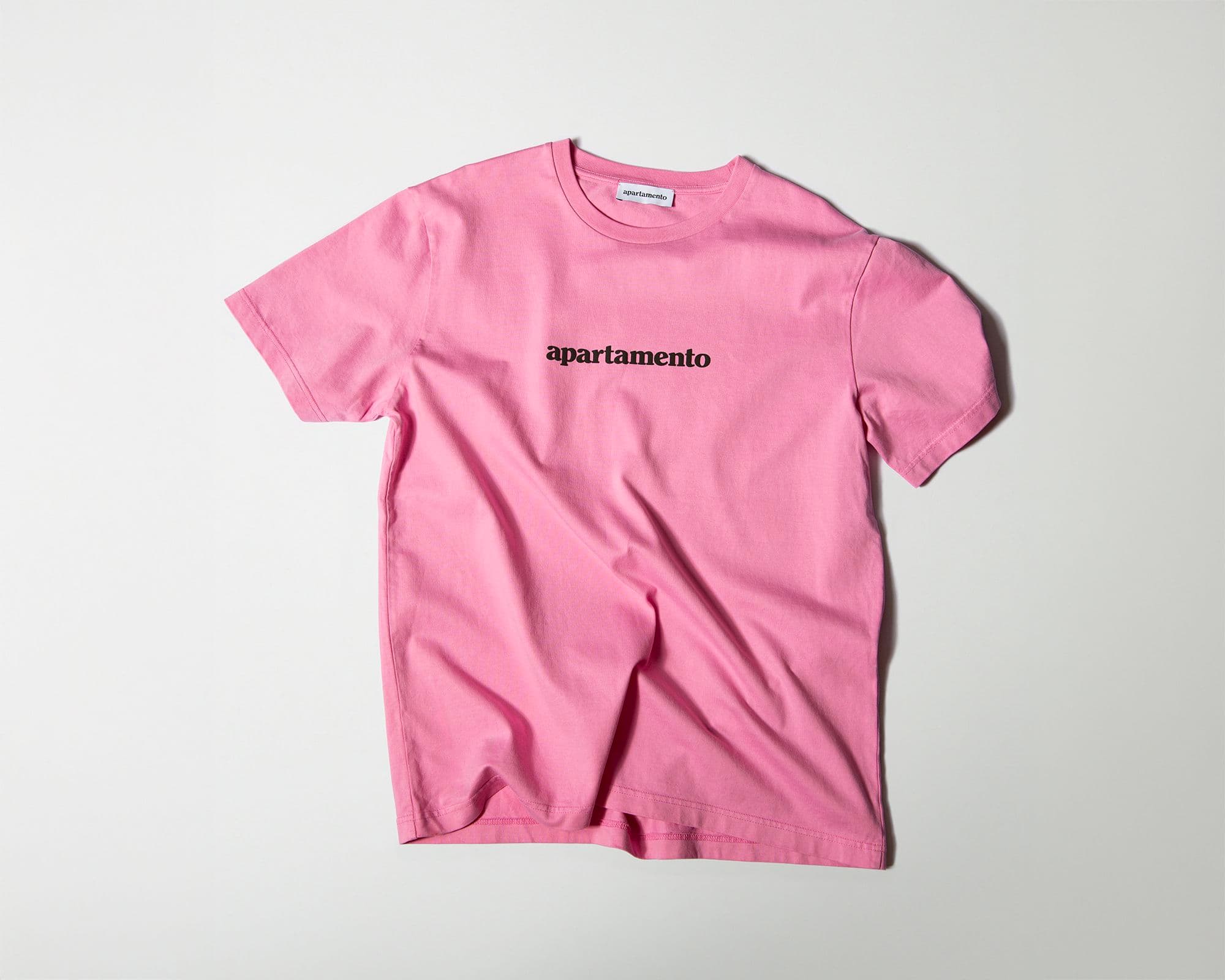 Pink T-shirt with "apartamento" printed in black on the front, displayed on a plain white background.