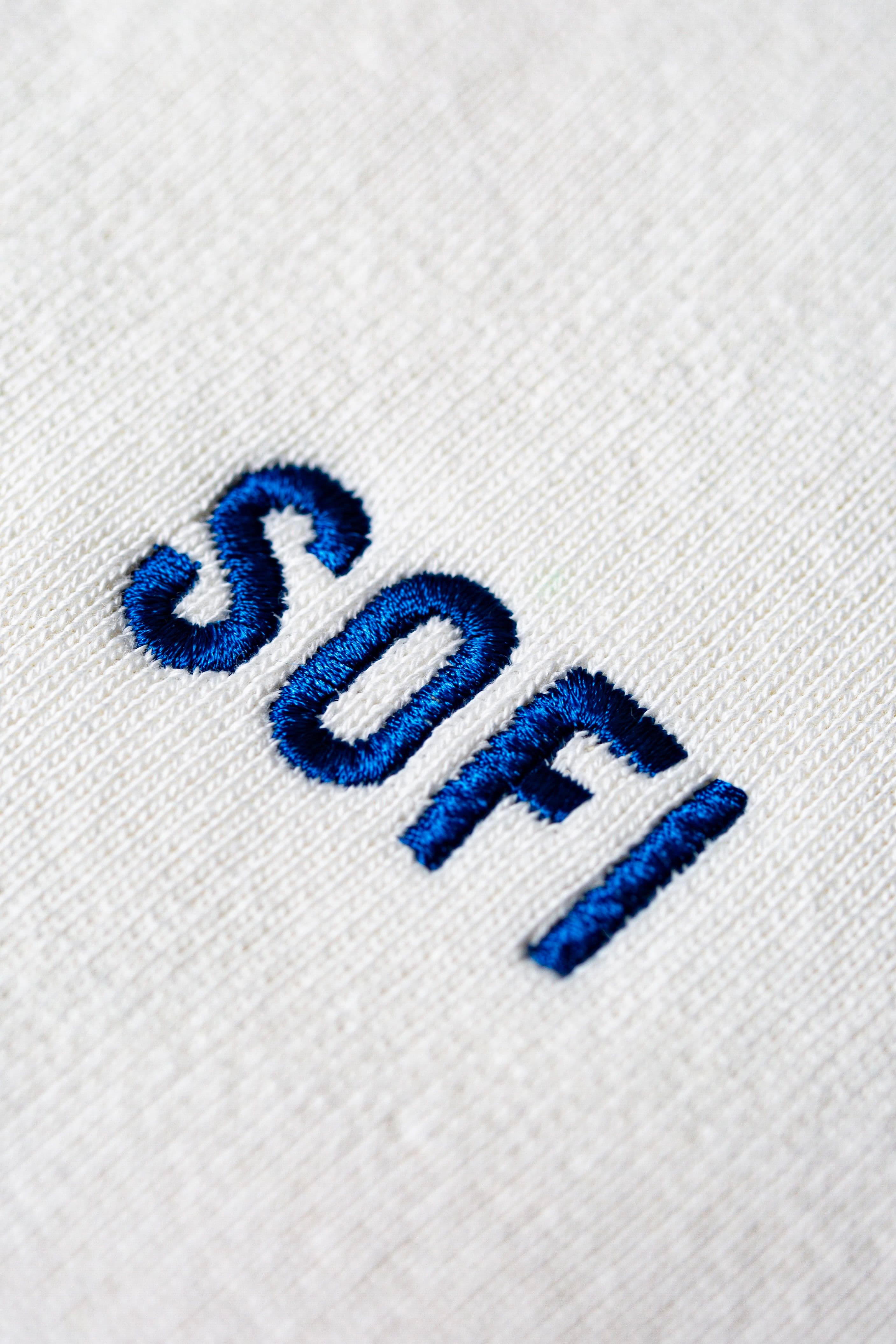 Close-up of the word "SOFI" embroidered in blue thread on a textured white fabric background.