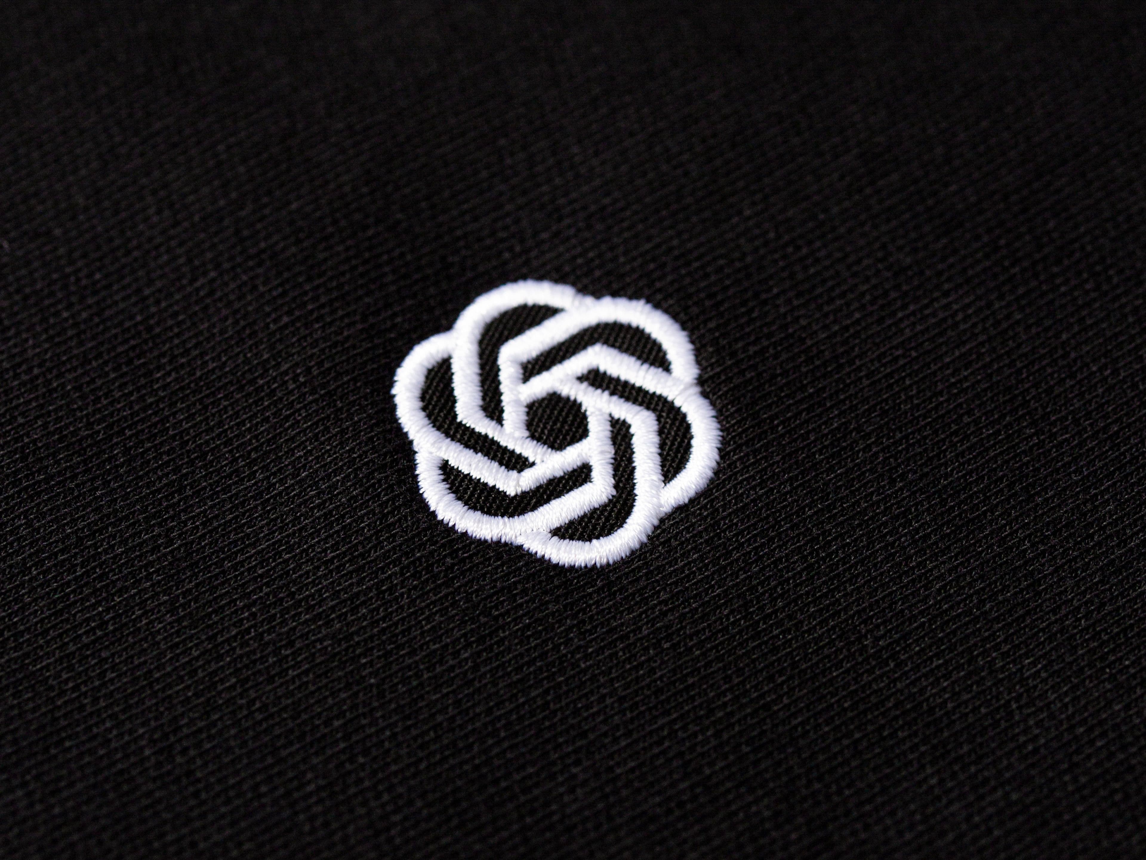 Close-up of white embroidered logo on black fabric showing fine stitched detail.