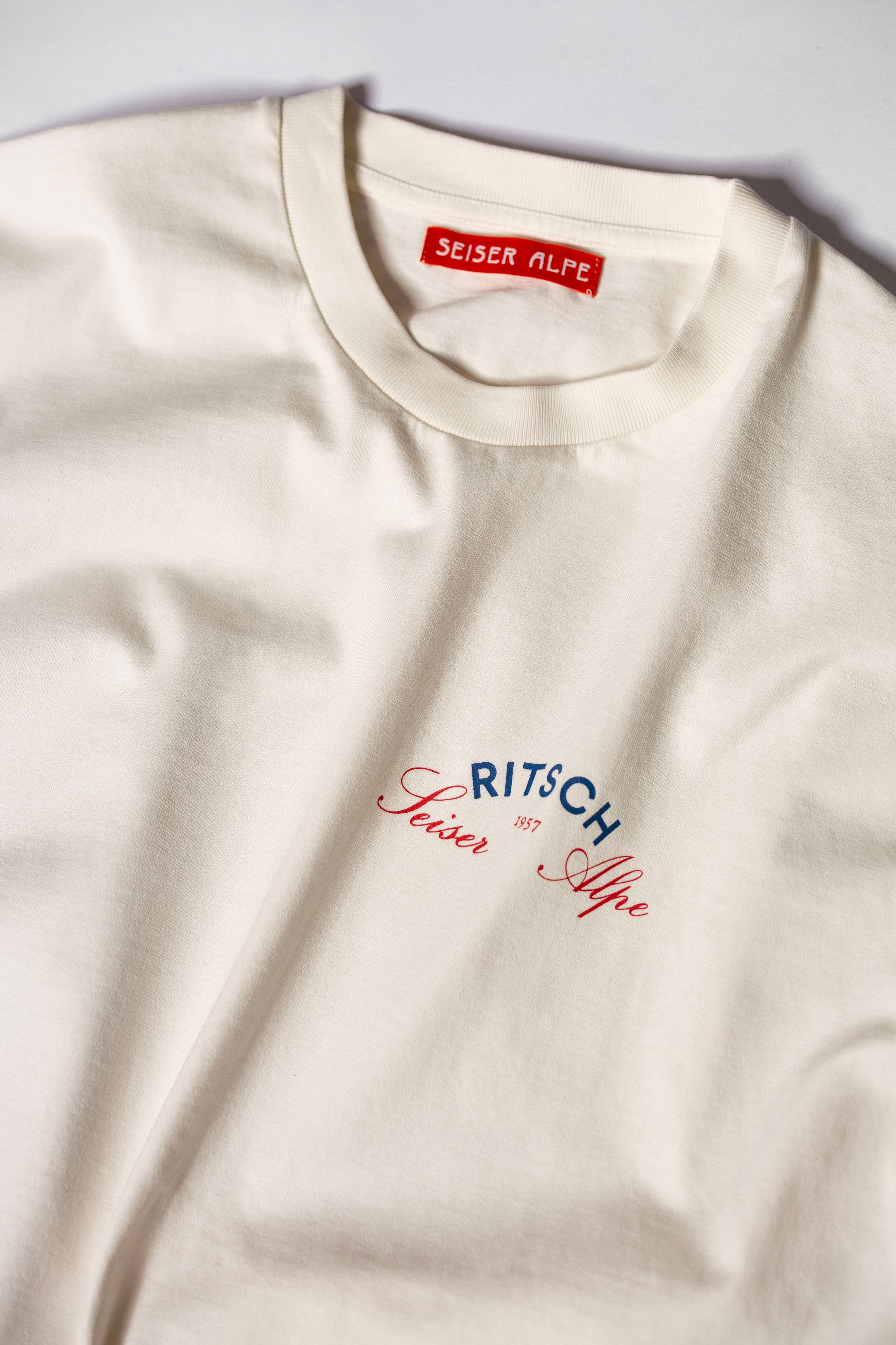 Close-up of a cream-coloured custom printed t-shirt with red woven neck label with words "Seiser Alpe" and detailed logo print.