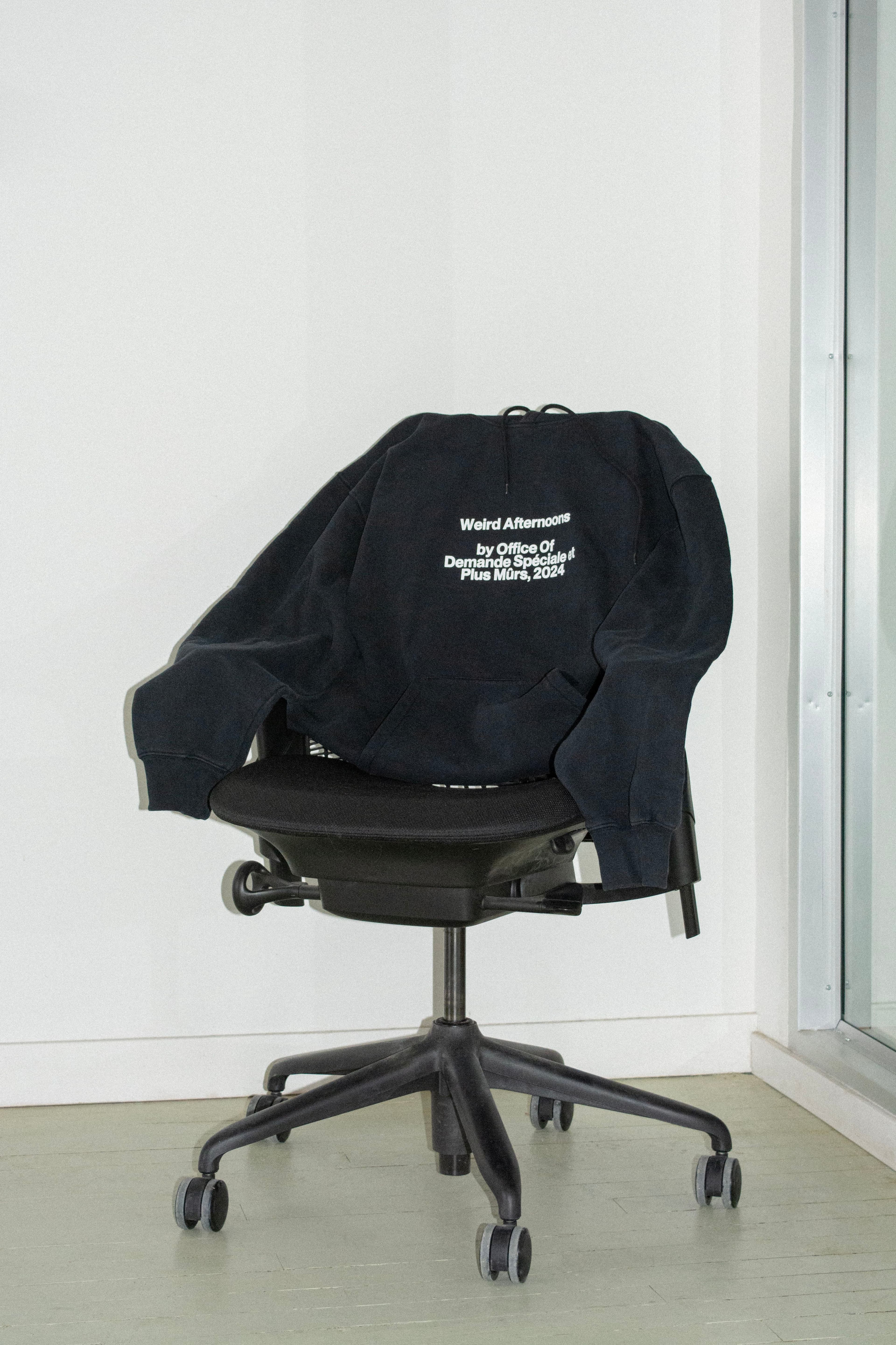 Black branded hoodie with words "Weird Afternoons" draped over an office chair, representing custom merch as part of everyday company culture.