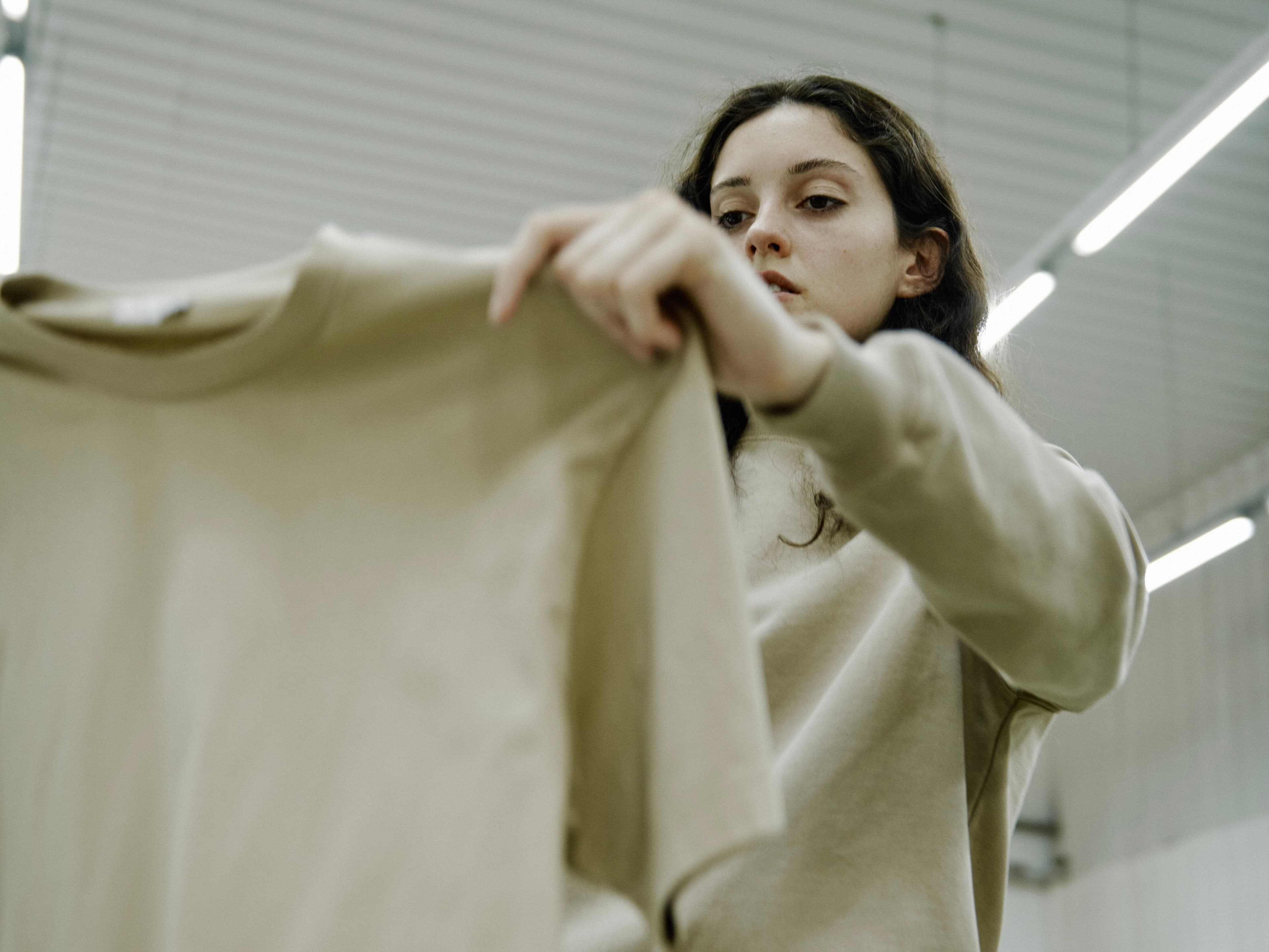 Assembly team member inspecting a beige garment dyed t-shirt during quality control, highlighting the premium standards of custom merch production.