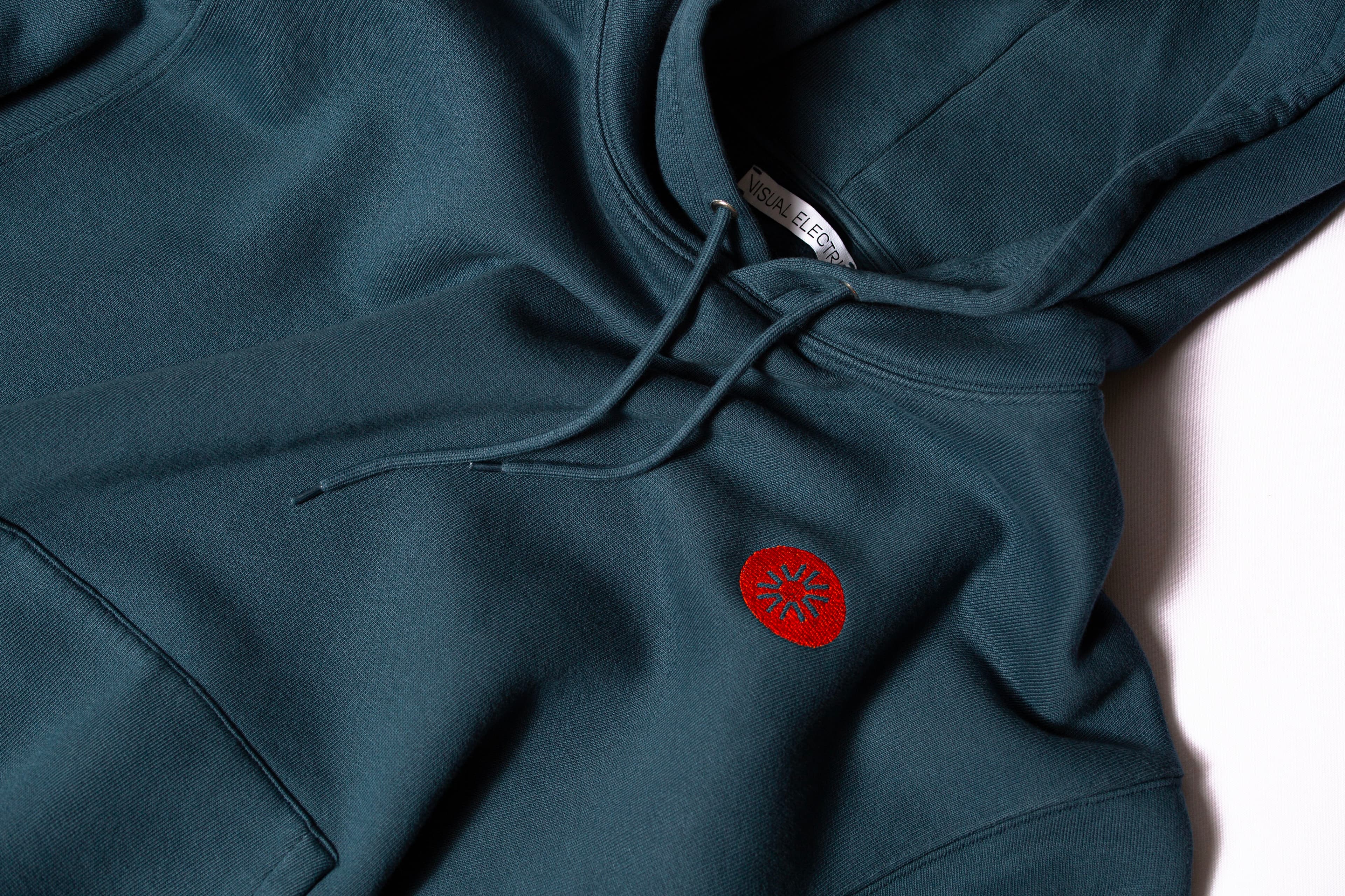 Blue hoodie with a small red embroidered circular logo and Visual Electric label.