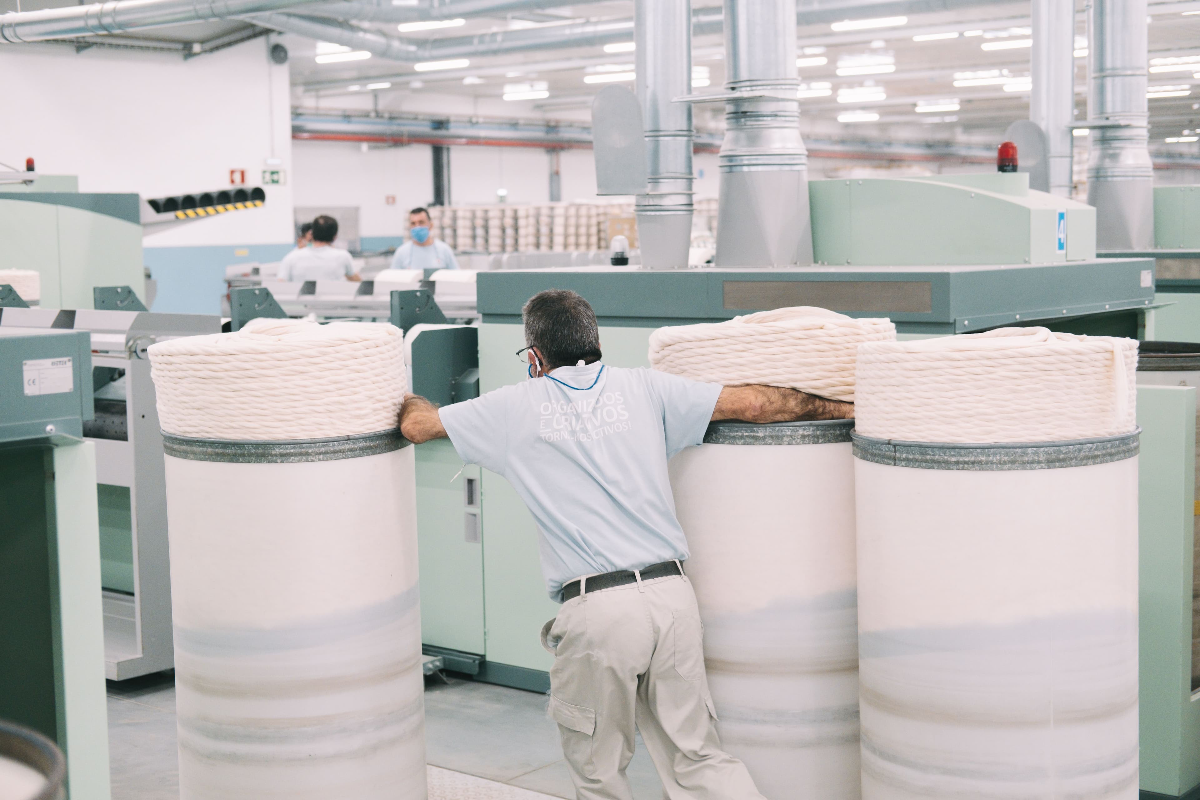 Worker handling large spools of organic cotton at Assembly’s production facility, highlighting sustainable practices in garment dyeing.