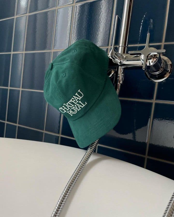 Green Château Royal custom embroidered cap placed on a bathtub with blue tiled wall background.