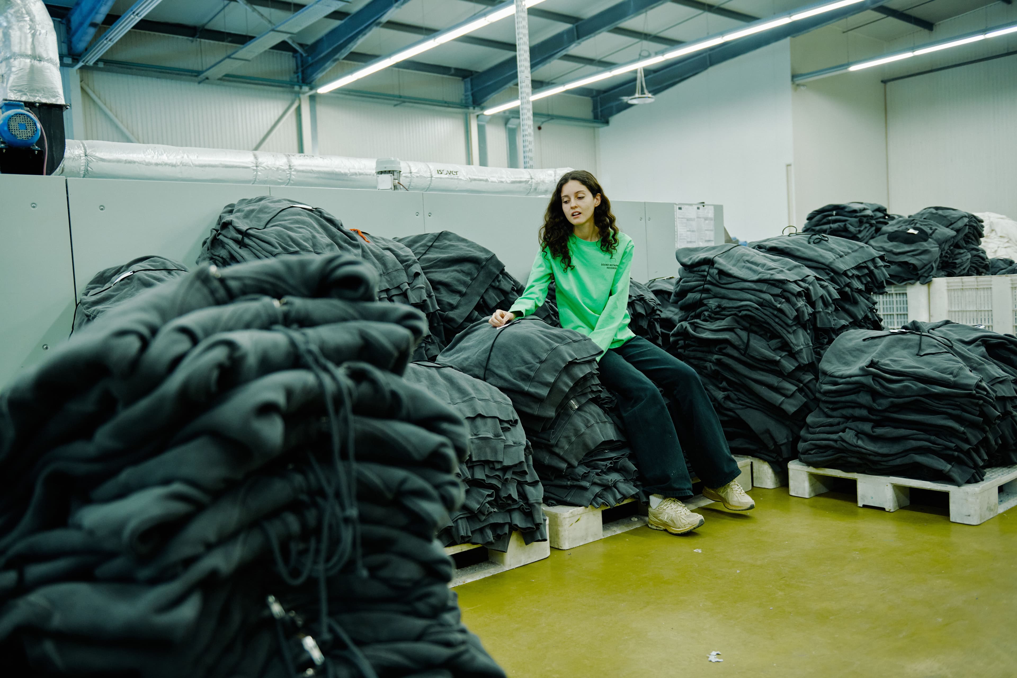 Team member wearing green sweatshirt with stacks of black hoodies inspecting them in a production facility.